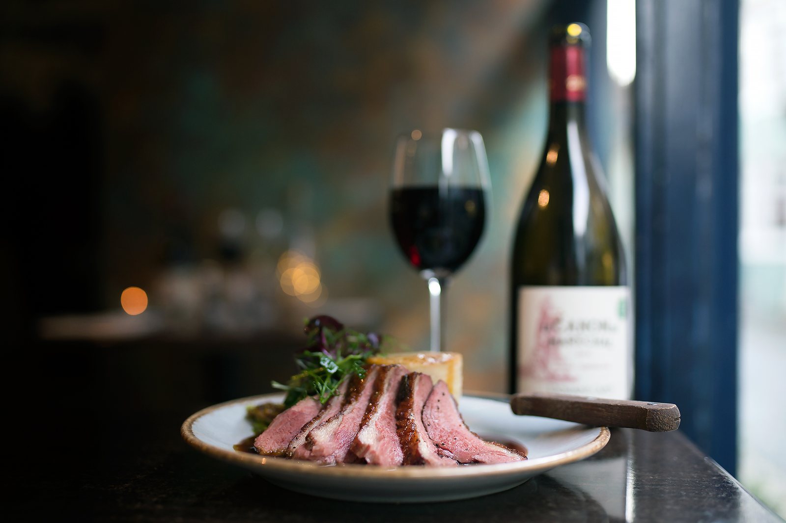 Sliced duck breast plated beside a glass of red wine
