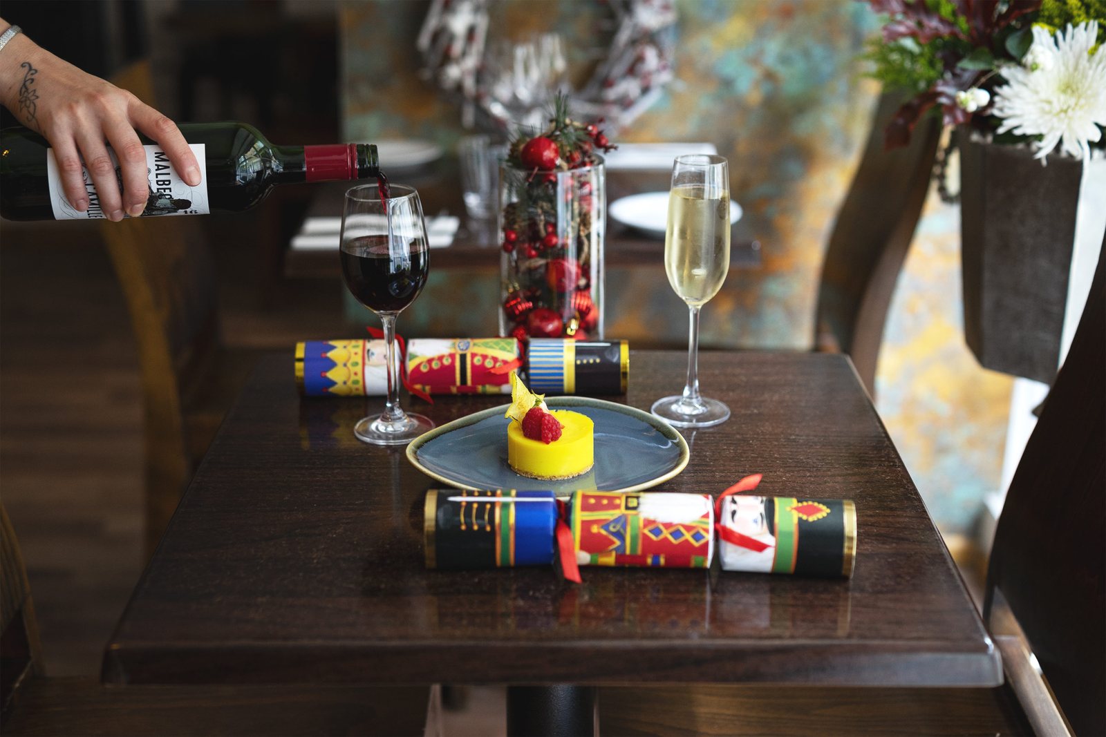Wine being poured over a laid table with flowers and a dessert