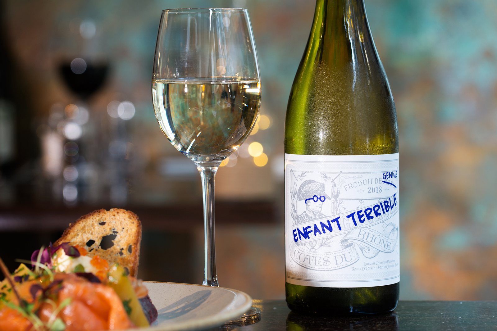 A glass of white wine and an open bottle beside a starter