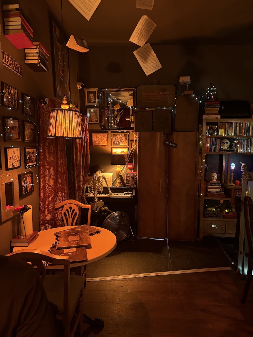Wall of framed vintage portraits above candles, books and a witch figurine